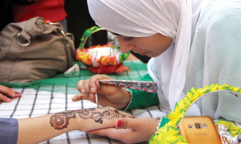 A girl applies henna on hand of a visitor at the exhibition. &mdash; Dawn