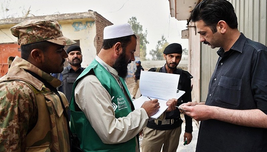 An official from the Pakistan Bureau of Statistics collects information from a resident during a census as security personnel guard them in Peshawar on March 15.— AFP