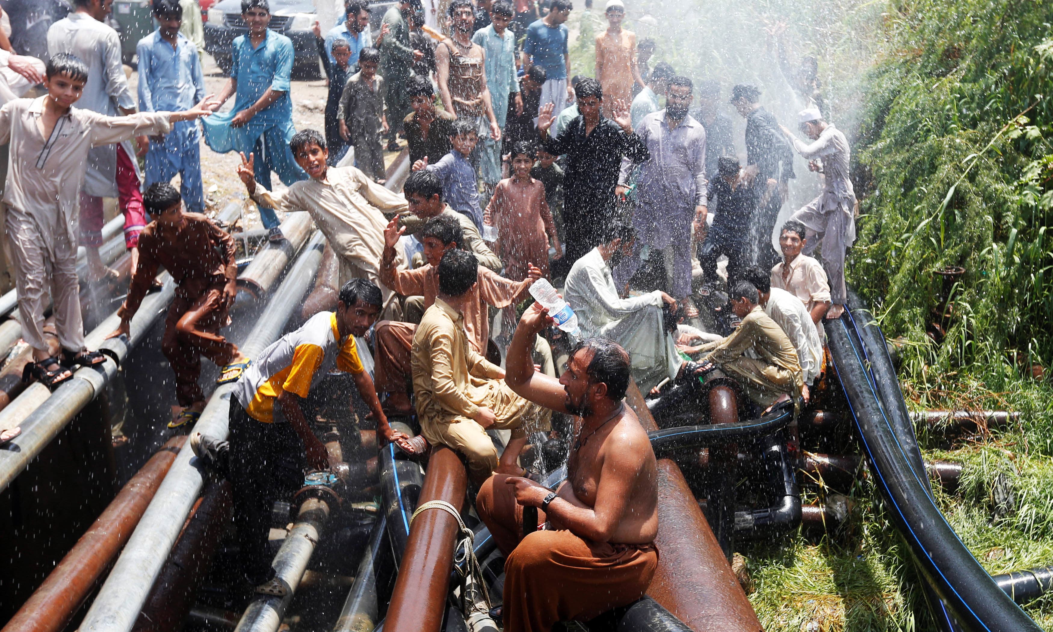 People cool off with water from lines after they punctured them in protest against the power outages in their area in Karachi. —Reuters