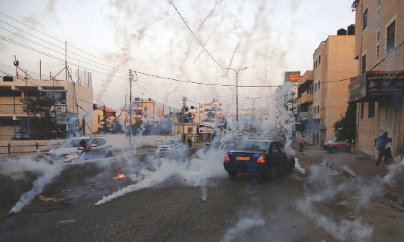 RAMALLAH: Palestinian men run for cover from tear gas during clashes between demonstrators and Israeli forces at the Qalandiya checkpoint, between Ramallah and Jerusalem, on Monday.─AFP