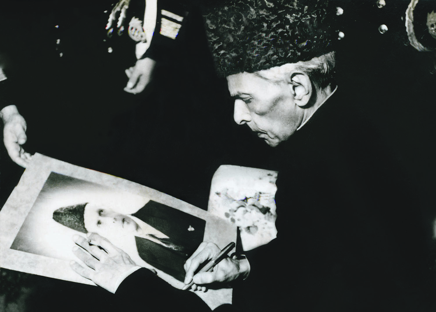 In this rare meta-image, Quaid-i-Azam Mohammad Ali Jinnah autographs his portrait at a reception held in Karachi in December 1947. | Photo: The Press Information Department, Ministry of Information, Broadcasting &amp; National Heritage, Islamabad (PID)