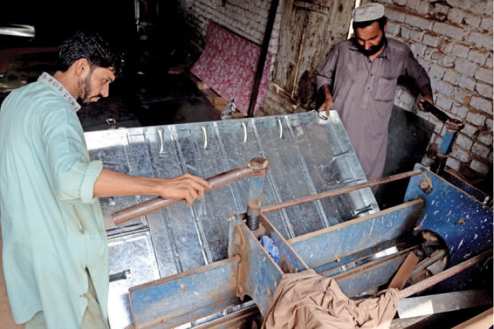 Workers use a machine to press steel sheets together to make a larger trunk, locally known as a paiti.