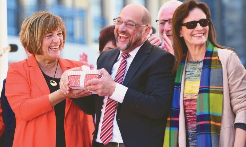 (left) German Chancellor Angela Merkel inspects vegetables at a harvest festival as she tours the city of Lauterbach on the Baltic Island of Ruegen. (right) Martin Schulz (centre), leader of Germany’s Social Democratic Party and candidate for Chancellor, and vice-president of the Bundestag (lower house of parliament) Ulla Schmidt (left) hold a present as Schulz wife Inge Schulz (right) looks on during an electoral meeting on the eve of the general elections in Aachen, western Germany.—AFP