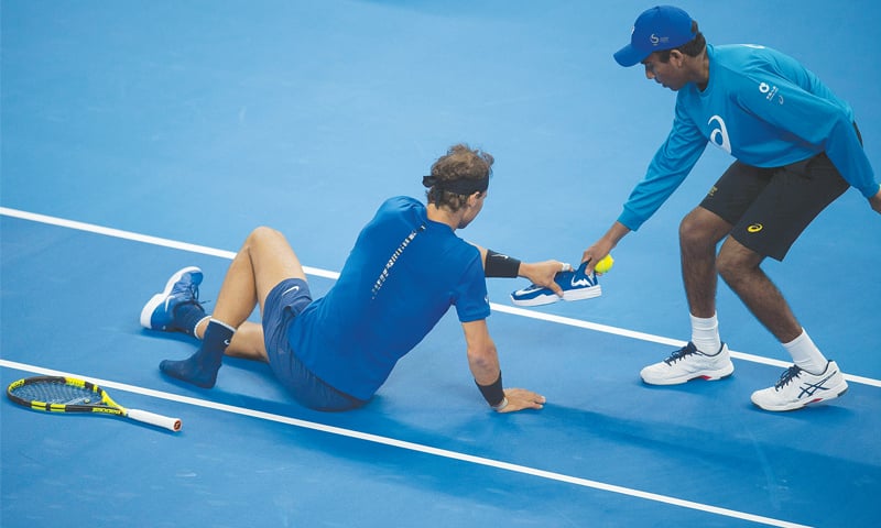 BEIJING: Rafael Nadal of Spain (L) receives his left shoe from a ball boy after he slipped and fell during his China Open men&rsquo;s singles match against Lucas Pouille of France on Tuesday.&mdash;AFP