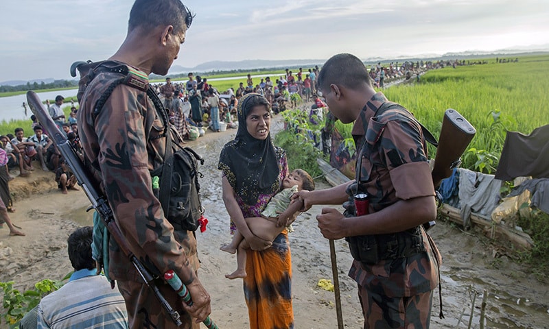 A newly arrived Rohingya woman holds her sick son as a Bangladesh border guard soldier checks him before allowing them to proceed forward to receive medical assistance.—AP