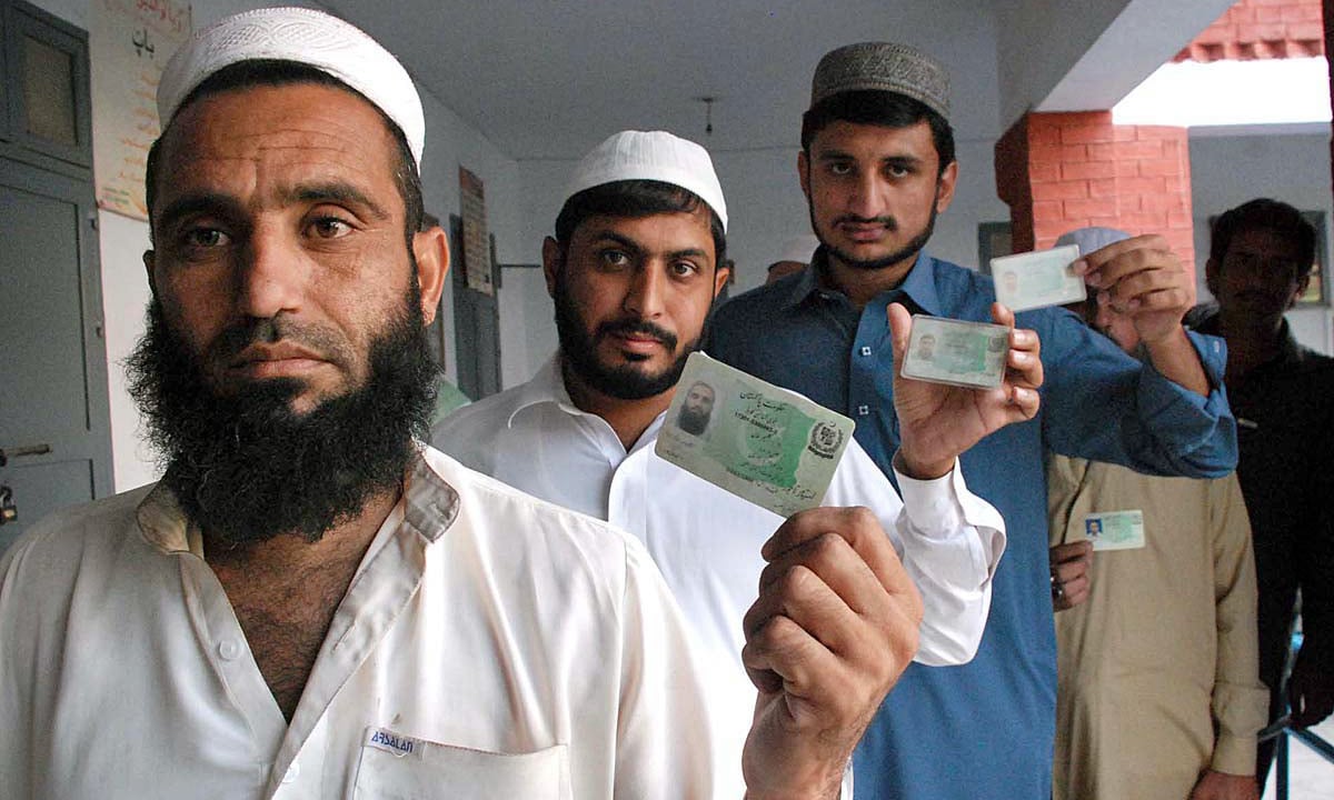 Voters showing their CNIC while standing in queue at polling station during by-election in NA-4 constituency. —APP