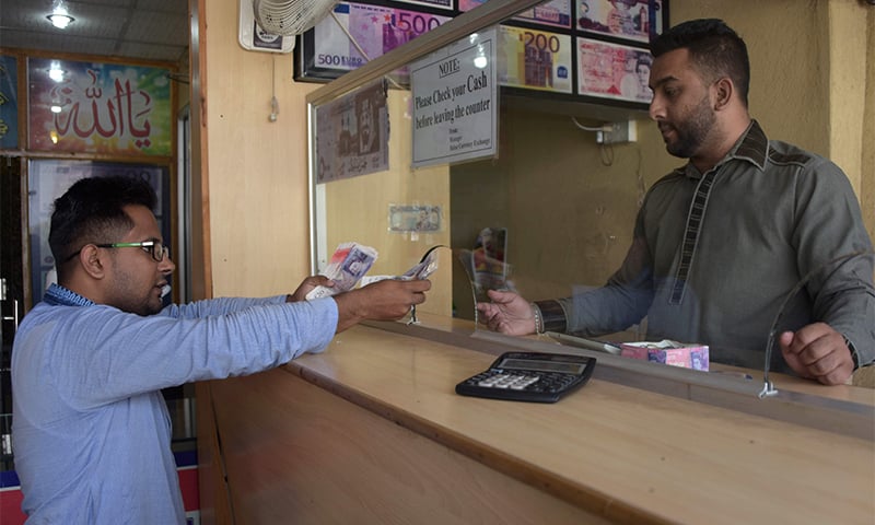 A visiting dual citizenship holder (L) exchanging British pounds at a remittance shop in Azad Jammu Kashmir's Mirpur. ─ AFP