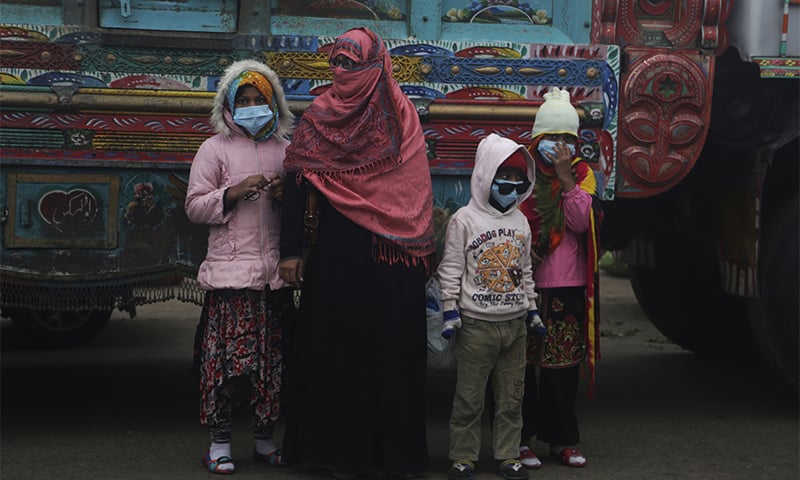 A family wears masks to protect from the smog while waiting for transport on the roadside in Lahore. ─ AP
