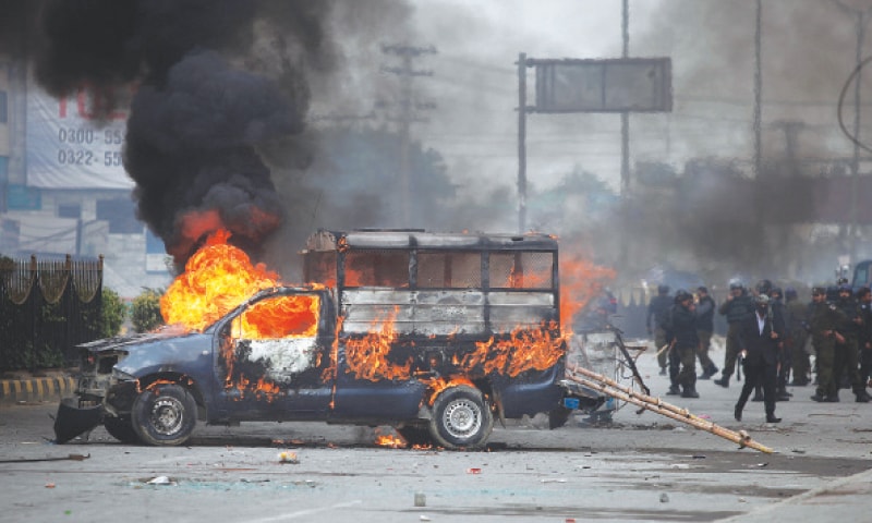 Islamabad: Policemen gather next to a burning police vehicle set on fire by protesters during a clash on Saturday.—AP