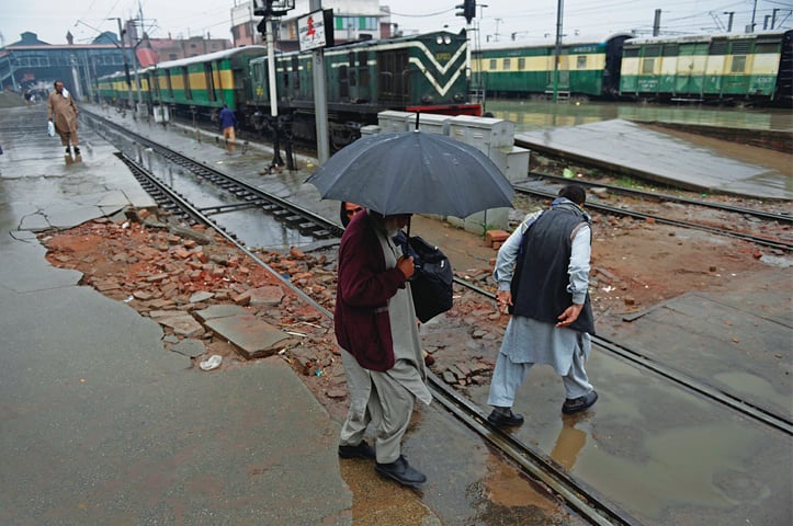 A man holding an umbrella crosses the track at the Lahore railway station during rain. &mdash; White Star
