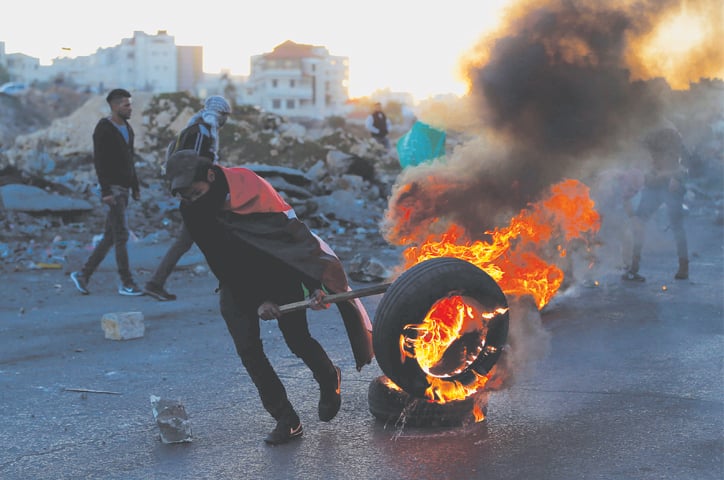 RAMALLAH: A Palestinian demonstrator burns a tyre during clashes with Israeli forces near a security checkpoint on Saturday.—AFP