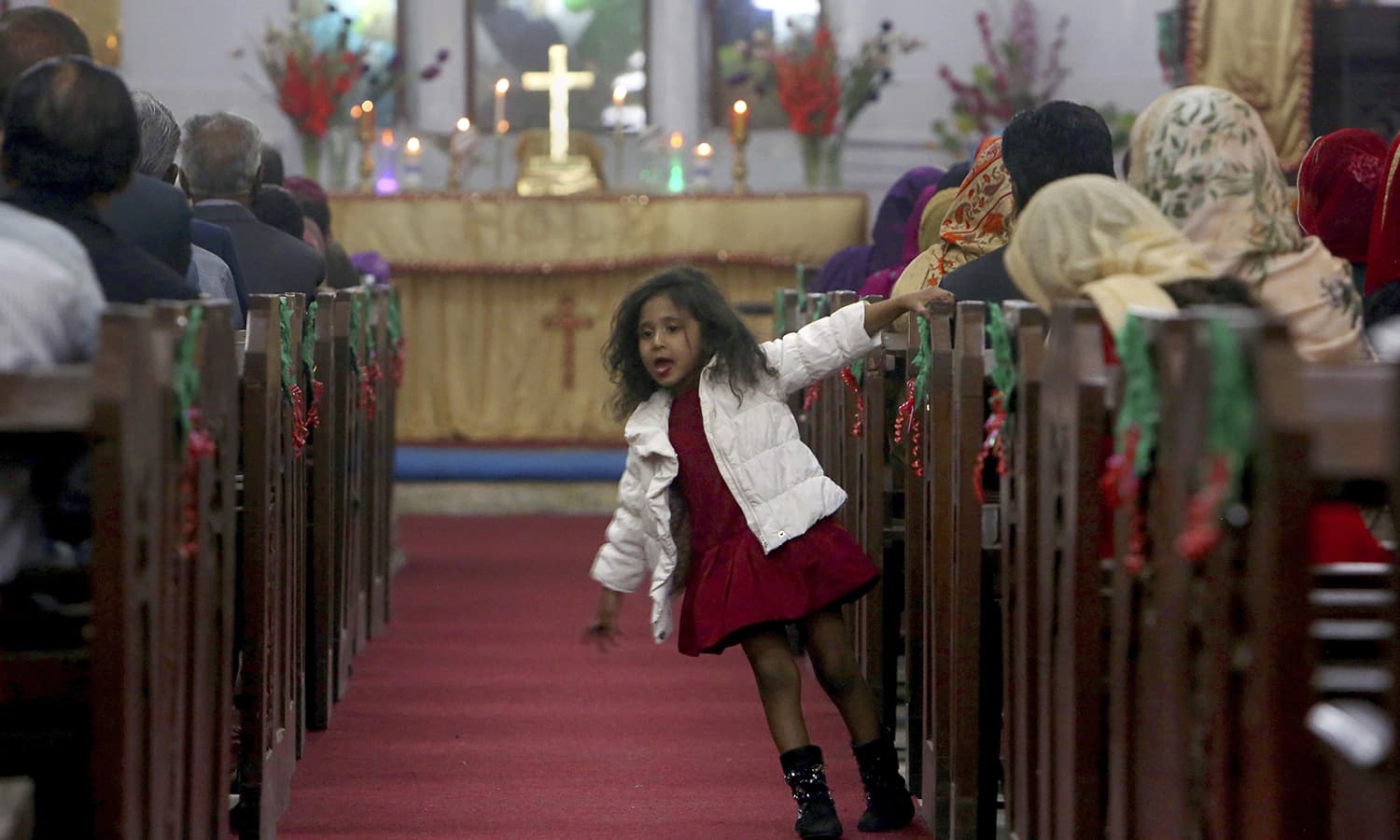 A Christian girl plays beside her mother attending midnight Christmas Mass at Christ church in Karachi. — AP