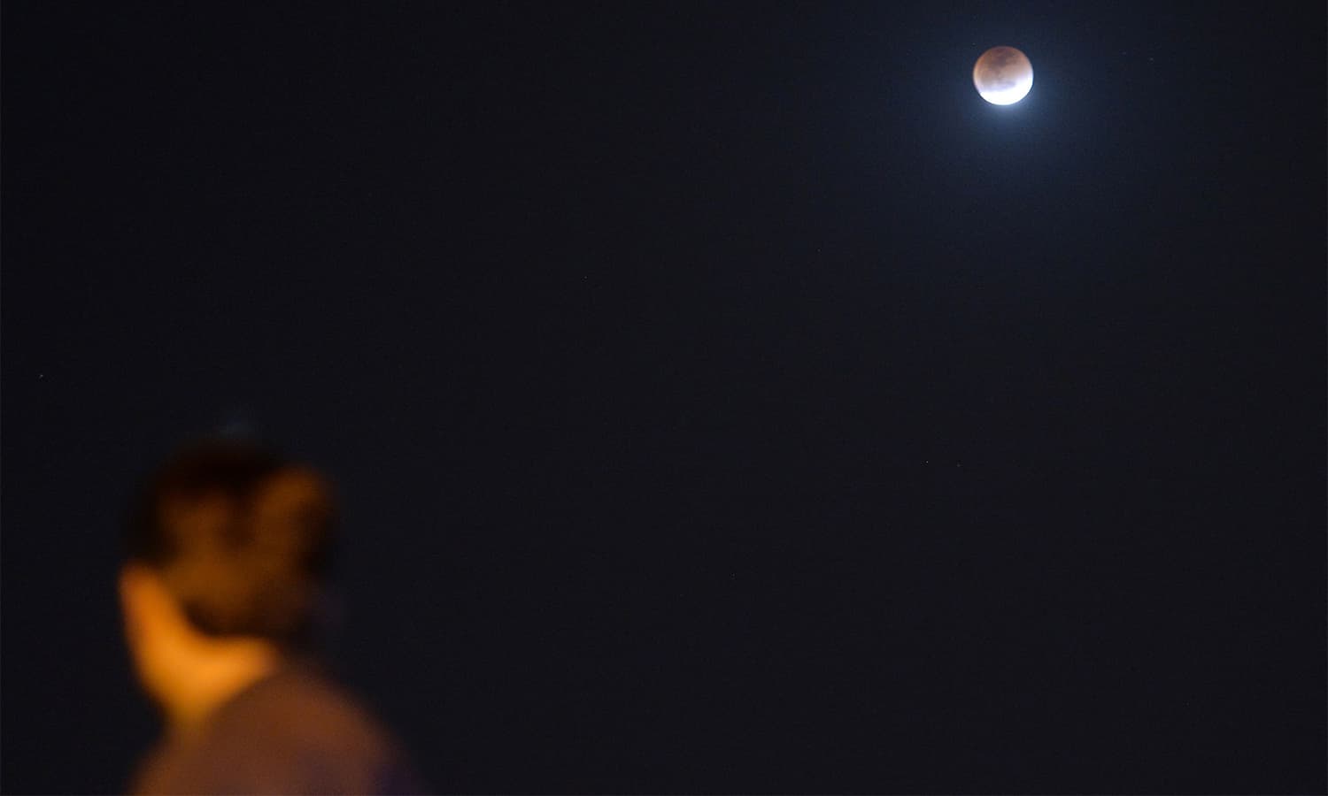 A resident watches the moon during a lunar eclipse in Islamabad.— AFP