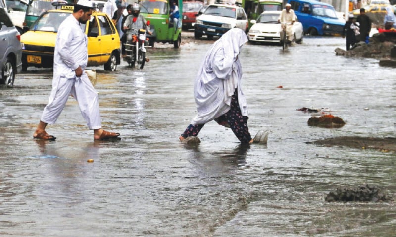 Pedestrians wade through rainwater at Stadium Chowk after heavy downpour in Peshawar on Sunday. &mdash; White Star