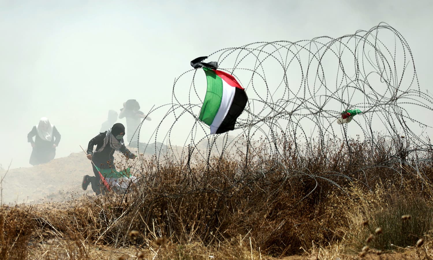 A Palestinian protester holding his national flag runs past barbed wires during clashes with Israeli forces near the border between the Gaza strip and Israel east of Gaza City. — AFP