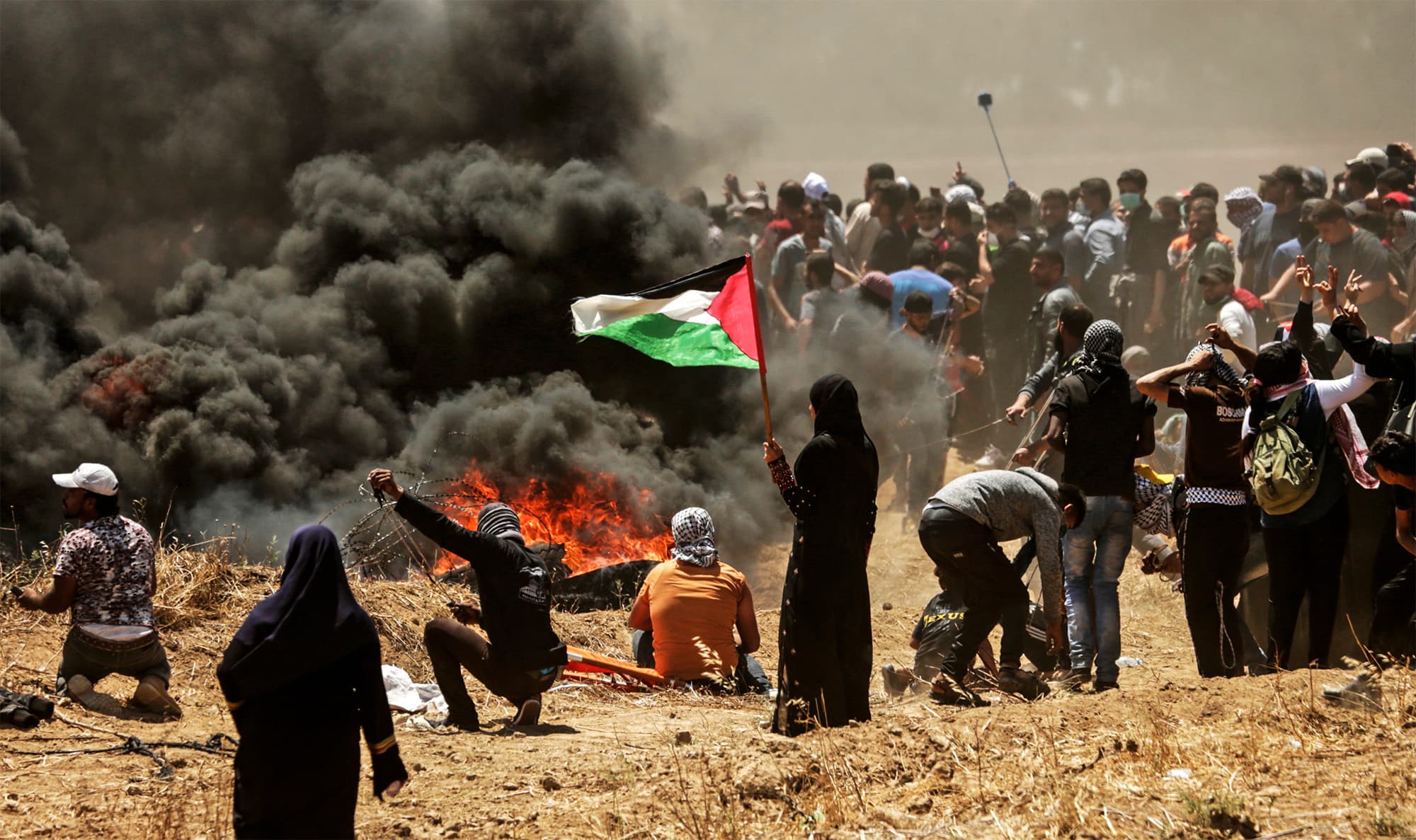 A Palestinian woman holding her national flag looks at clashes with Israeli forces near the border between the Gaza strip and Israel on May 14, 2018. — AFP