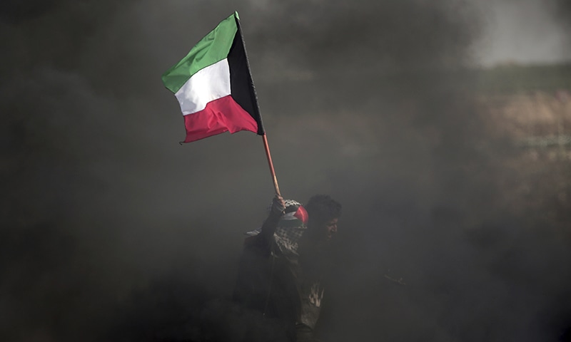 A Palestinian woman holds Kuwaiti flag during a protest at the Gaza Strip's border with Israel. —AP