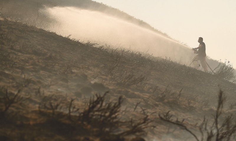STALYBRIDGE (Britain): Firefighters dampen the moorland wildfire with water on the hills on Wednesday.&mdash;AFP