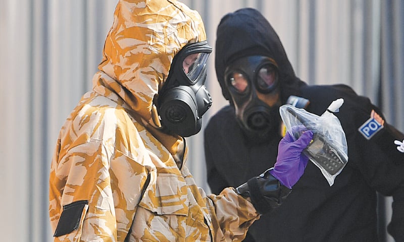 AN investigator wearing a camouflaged protective suit, gloves and a gas mask works with a policeman in protective suit outside the John Baker House Sanctuary Supported Living in Amesbury, southern England, on Friday.&mdash;AFP