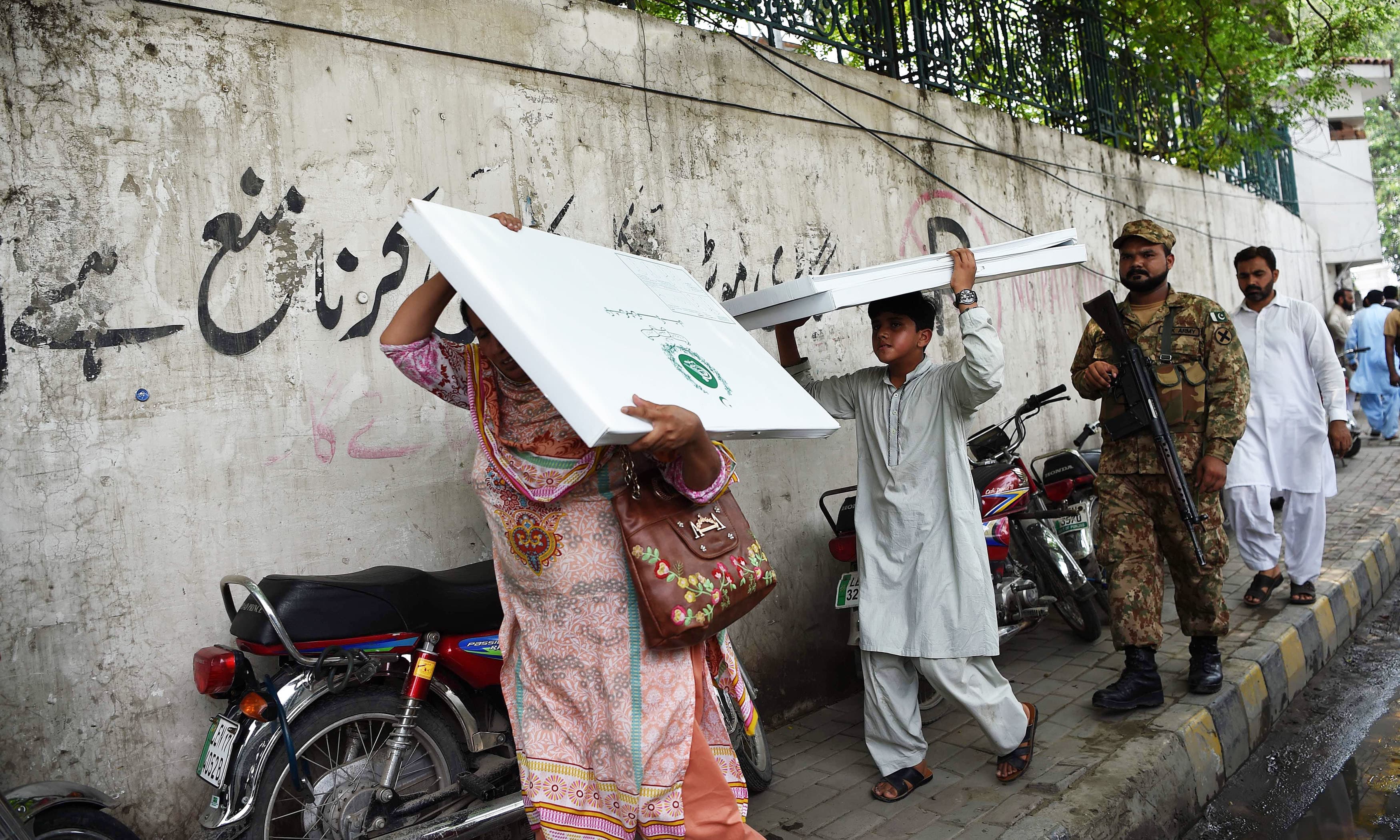 Polling official carries election material as a soldier escorts her in Lahore. —AFP