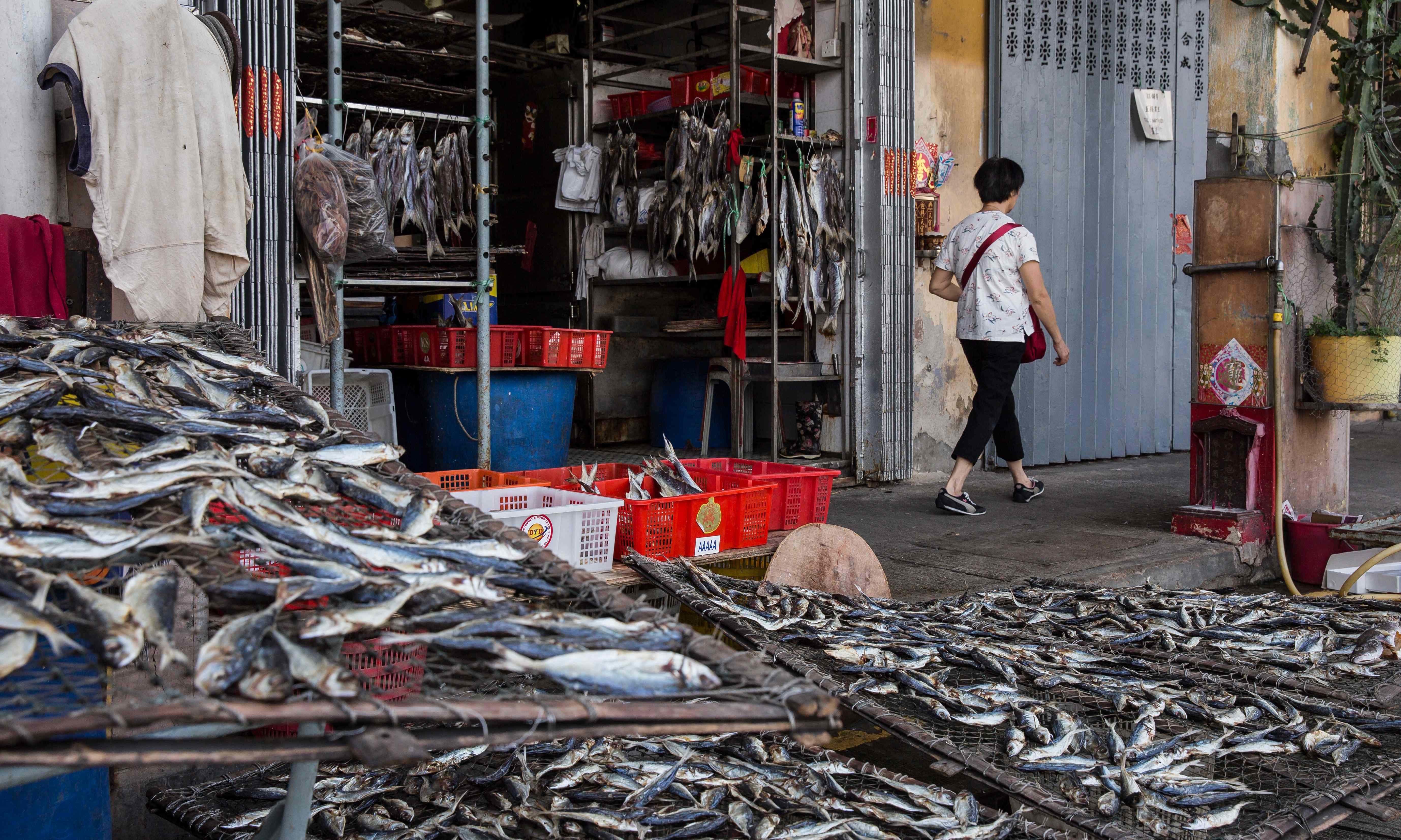 A pedestrian (R) walks past a shop selling dried fish before the expected arrival of Super Typhoon Mangkhut in Macau — AFP