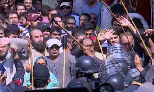 Baton-wielding policemen in riot gear push back protesters in Karachi's Pakistan Quarters area. ─ DawnNewsTV
