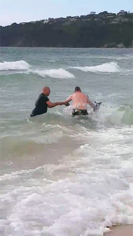 Police officers try to rescue a kangaroo struggling in the sea at Safety Beach in this still image taken from a video.—Reuters