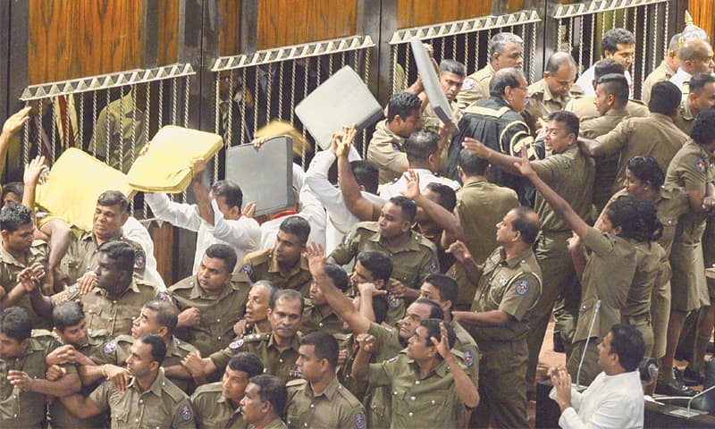 Colombo: Police escort Sri Lanka’s parliament speaker Karu Jayasuriya (top-right, in black and gold) as aides hold up cushions to protect him and themselves from projectiles thrown by rival legislators in the assembly hall on Friday. Sri Lanka’s political crisis escalated with the sacked prime minister demanding his job back shortly after passing another no-confidence motion against his controversial successor amid unprecedented rioting in parliament.—AFP            Report on Page 14