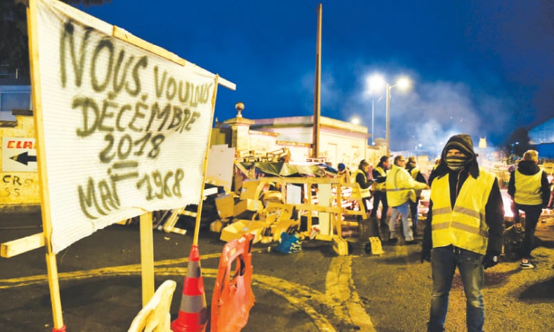 A YELLOW Vest protester (Gilets Jaunes) looks at a banner reading ‘We want December 2018 = May 1968’ (in reference to the civil unrest during May 1968) on a barricade blocking the access to the oil depot in Le Mans, northwestern France.—AFP