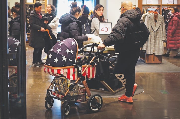 BEIJING: A Chinese man holds a baby stroller with an American flag design as he and his family members visit at a fashion boutique on Tuesday. China’s legislature is considering a law to prohibit government officials from pressuring foreign companies to hand over technology, a practice that helped spark Washington’s tariff war with Beijing. -AP