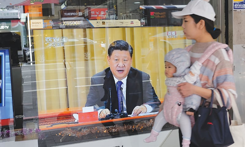 TAIPEI CITY: A mother carries her child past a television set showing China’s leader Xi Jinping making a speech on Wednesday in which he warned against efforts to promote the island’s independence.—AFP