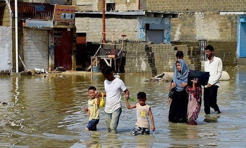 A family makes their way on a flooded street after heavy rain in Karachi in 2017. ─ AFP/File