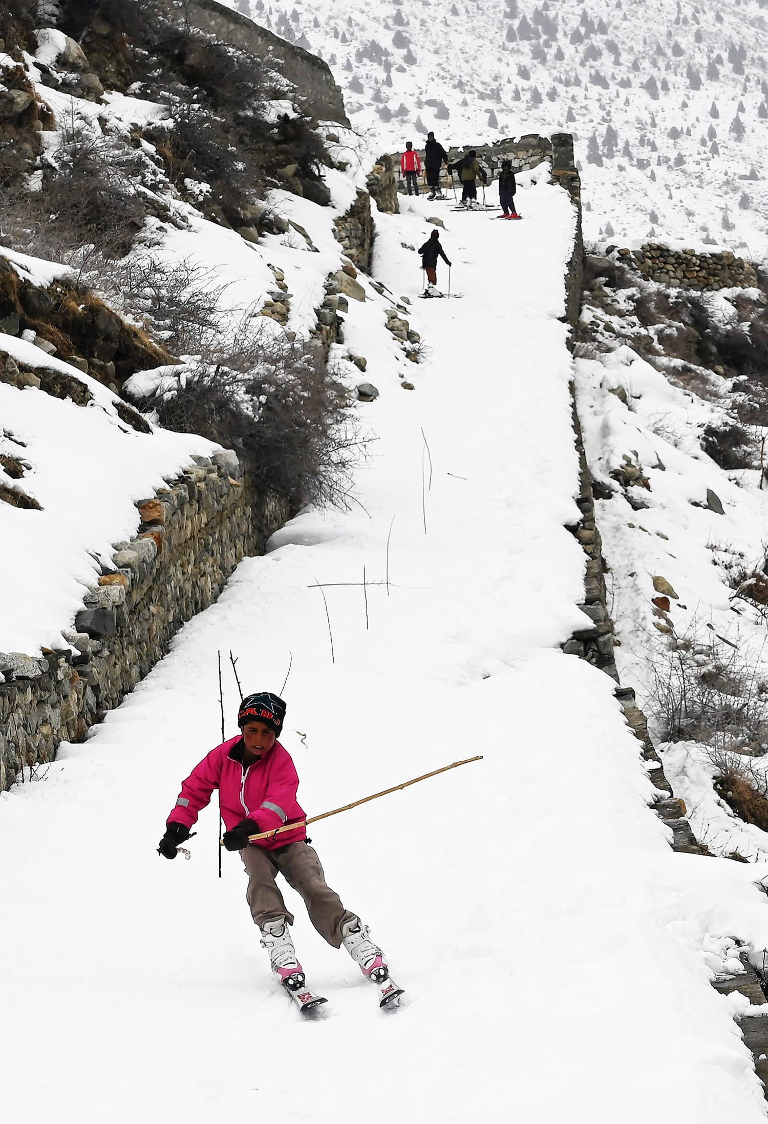 Children ski on a snow-covered street ─ with wooden sticks set up to practice the slalom ─ next to their homes near the slopes. ─ AFP