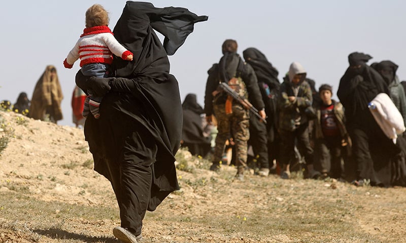A Syrian woman wearing a niqab walks carrying a child with other women who are fleeing the battered IS-held holdout of Baghouz in the eastern Syrian province of Deir Ezzor, into a nearby area held by the Syrian Democratic Forces (SDF) on February 12, 2019. ─ AFP