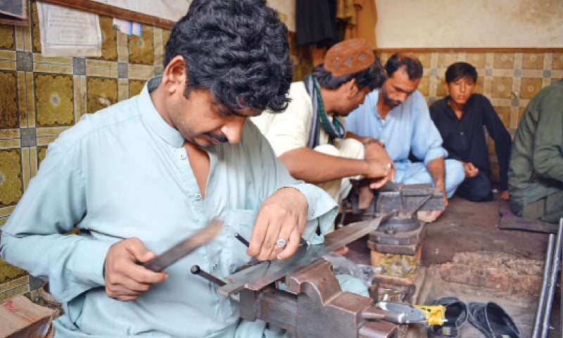 Artisans engrave patterns on weapons at a workshop in Dara Adamkhel arms market. &mdash; Dawn