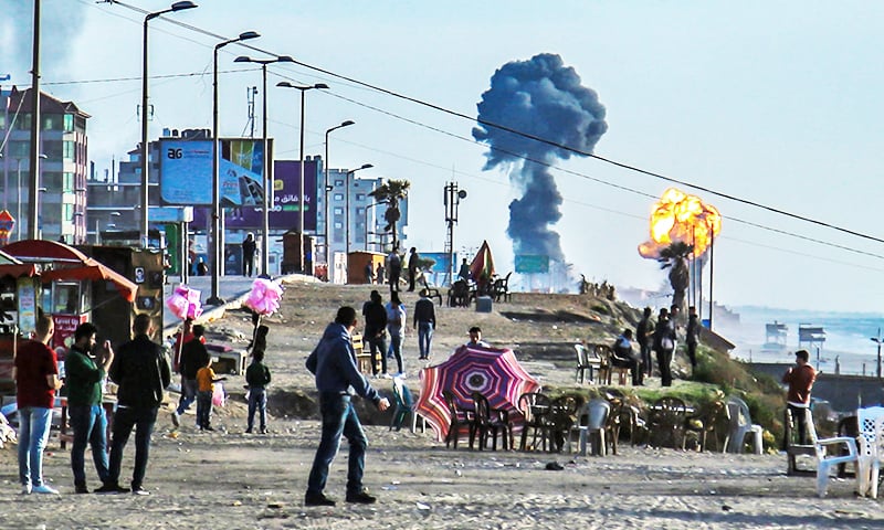 Palestinians gather on the beach in Gaza City as smoke and fire billow following  airstrikes by Israel. — AFP