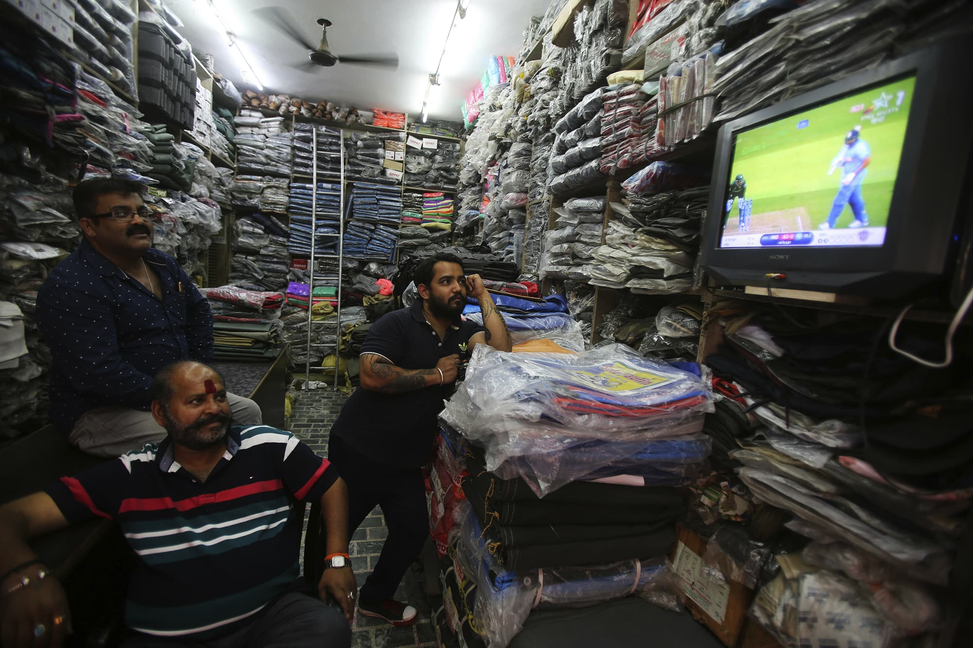 Men working at a textile shop in Jammu, IoK, watch the match on TV. ─ AP