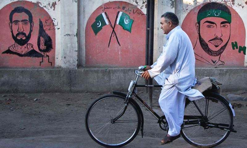 In this file photo, a Kashmiri man cycles past graffiti images of Burhan Wani.— AP