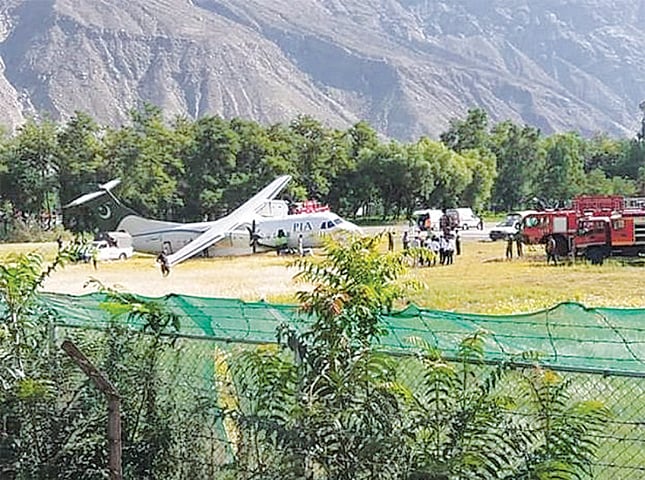 PASSENGERS and Civil Aviation Authority staff gather near the PIA aircraft after it skidded off the runway while landing at Gilgit airport on Saturday.—Dawn