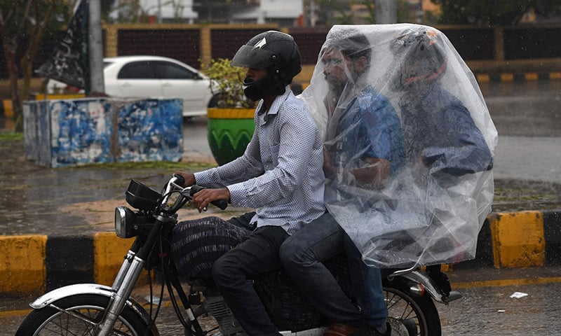 A Pakistani motorcyclist rides on a street as their passengers try to keep dry under plastic covering during monsoon rain in Karachi on July 29. — AFP