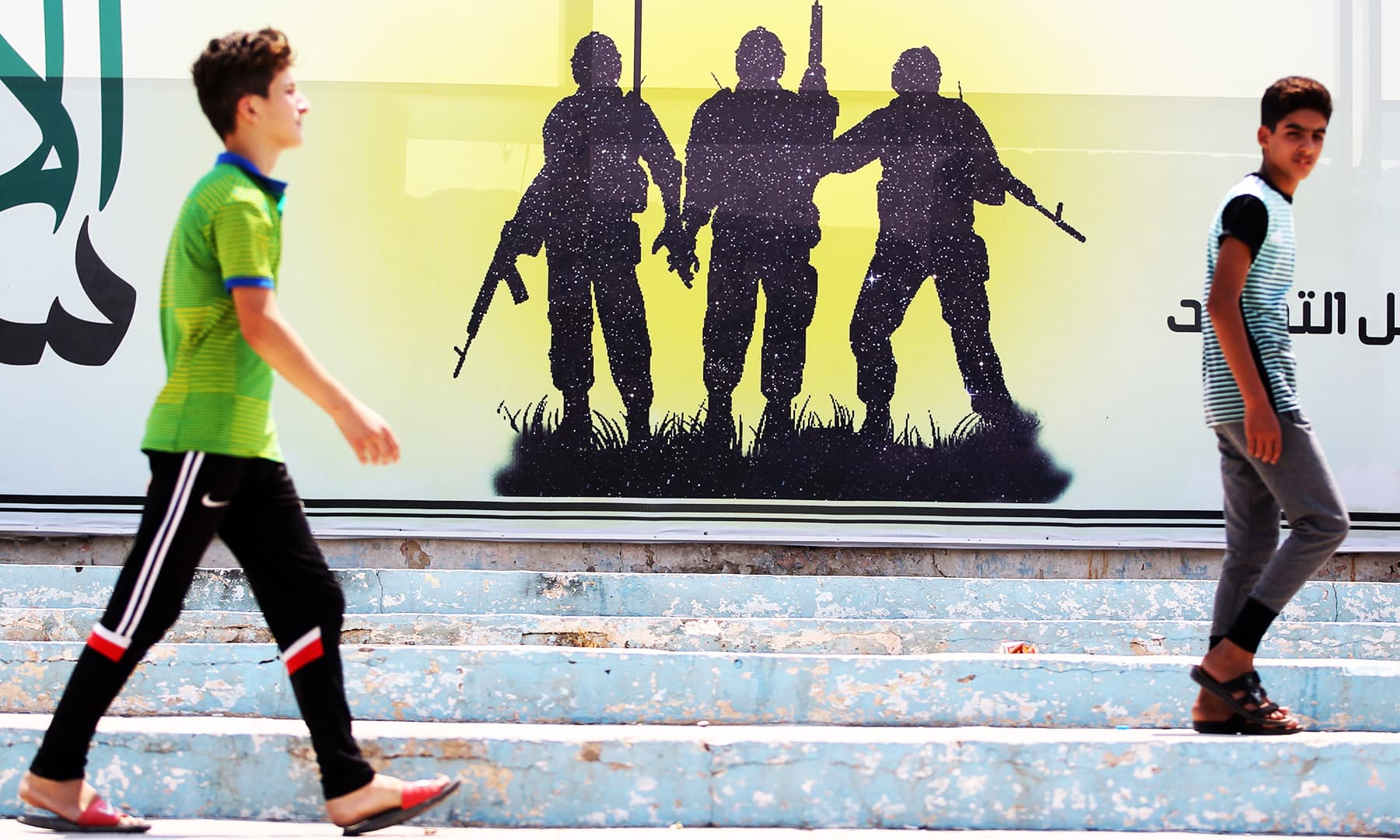 Youths walk past a banner depicting a silhouette of fighters with assault rifles in the Iraqi capital Baghdad's eastern suburb of Sadr City. &mdash; AFP