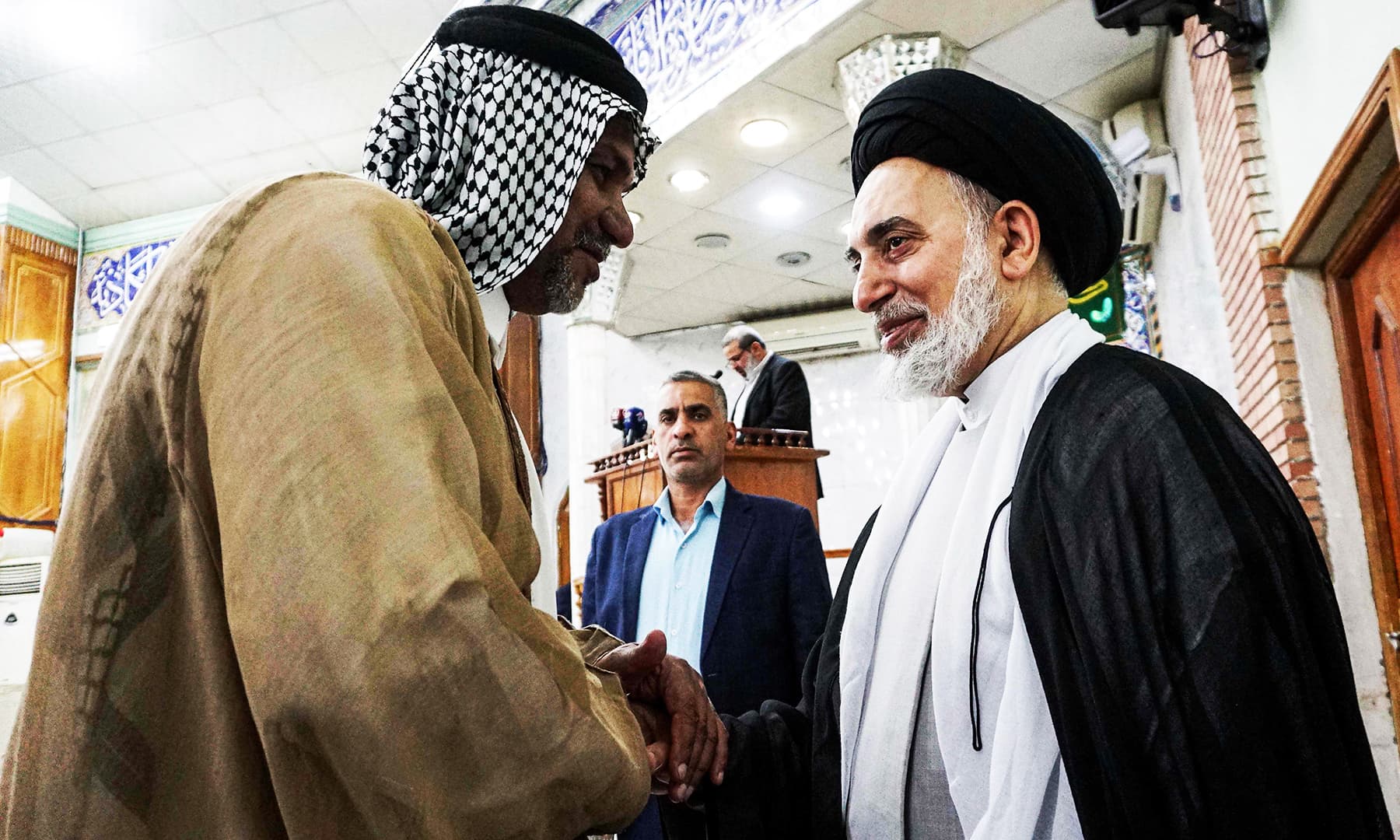 A man shakes hands with a Shia cleric while at a mosque for Eidul Azha prayers, in the central Iraqi shrine city of Najaf south of the capital on Monday. &mdash; AFP