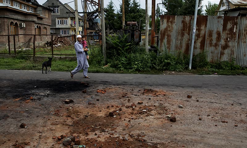 A Kashmiri man carries a child and walks on a road dotted with stones and bricks from earlier protests in Srinagar. ─ AP