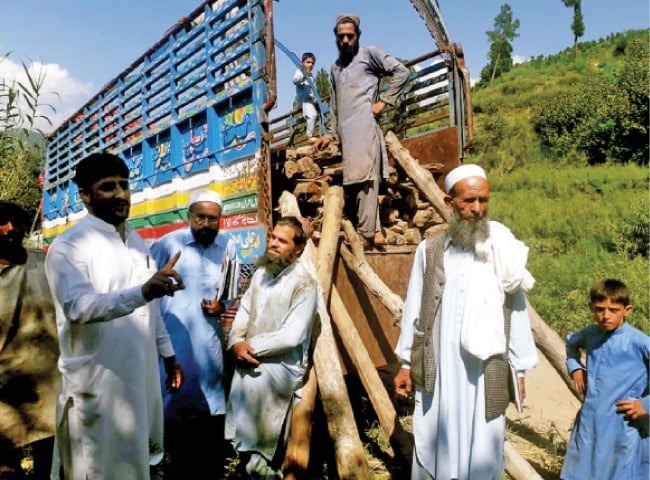 Afghan refugees load wooden logs from their demolished mud houses at Ichrian camp. — Dawn