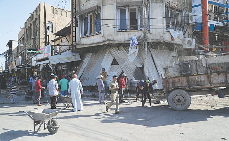 BAGHDAD: Municipality workers clean up as civilians inspect the aftermath a day after a motorcycle rigged with explosives exploded in Mussayyib, south of Baghdad.—AP