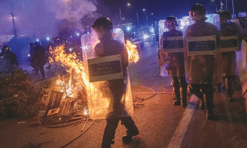 BARCELONA: Riot police units walk past a barricade on fire during a demonstration at El Prat airport, on the outskirts of Barcelona.—AP