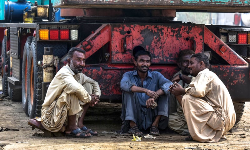 Four labourers sit in the shade of a truck in Karachi