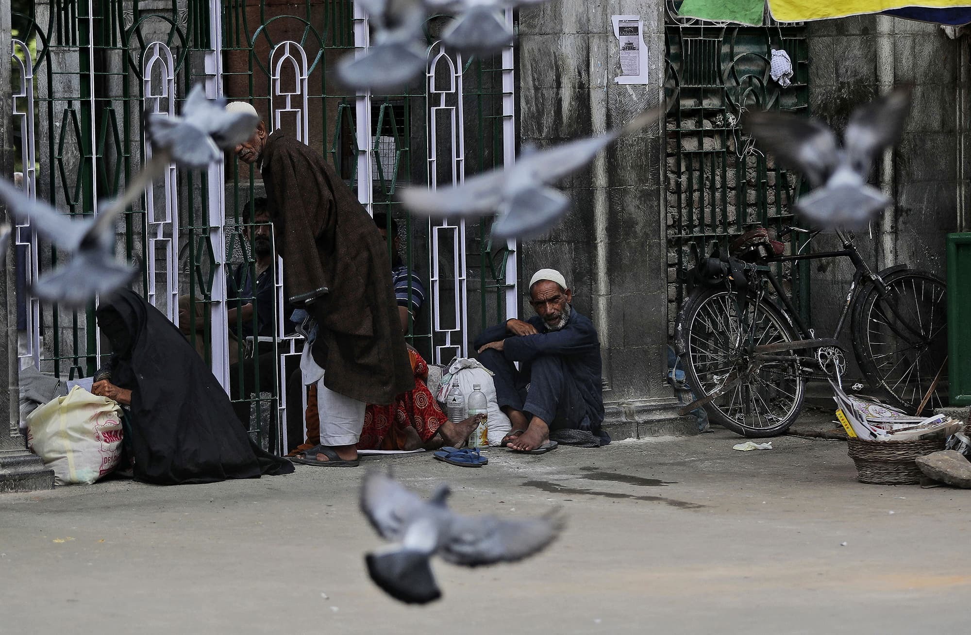 In this Friday, Aug. 9, 2019, photo, Kashmiris sit outside a Muslim shrine during a curfew in Srinagar, Indian controlled Kashmiri. Authorities enforcing a strict curfew in Indian-administered Kashmir will bring in trucks of essential supplies for an Islamic festival next week, as the divided Himalayan region remained in a lockdown following India's decision to strip it of its constitutional autonomy. The indefinite 24-hour curfew was briefly eased on Friday for weekly Muslim prayers in some parts of Srinagar, the region's main city, but thousands of residents are still forced to stay indoors