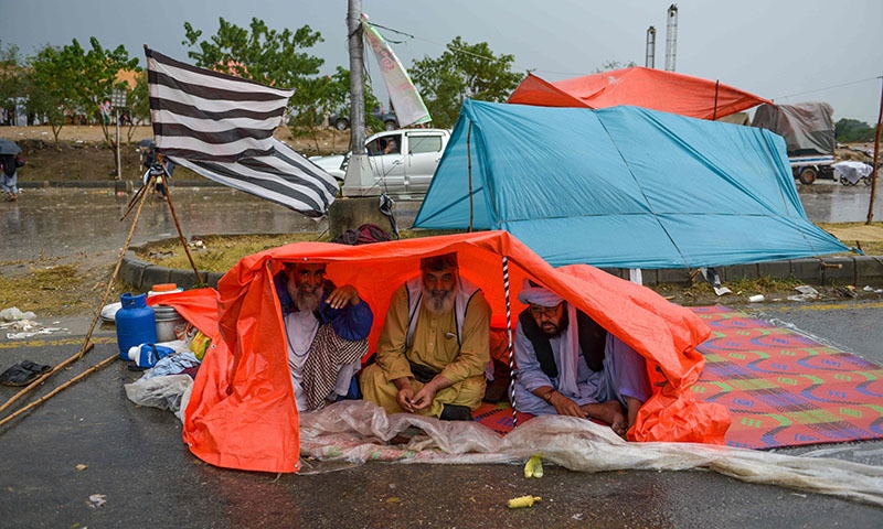 Azadi March participants look on as they sit in a shelter under the rain on November 6. — AFP