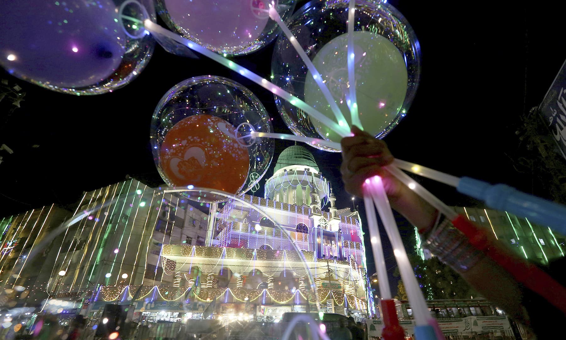 A street vendor holds lighted balloons next to a mosque, decorated with lights for Eid-i-Miladun Nabi, in Karachi, on Saturday. — AP